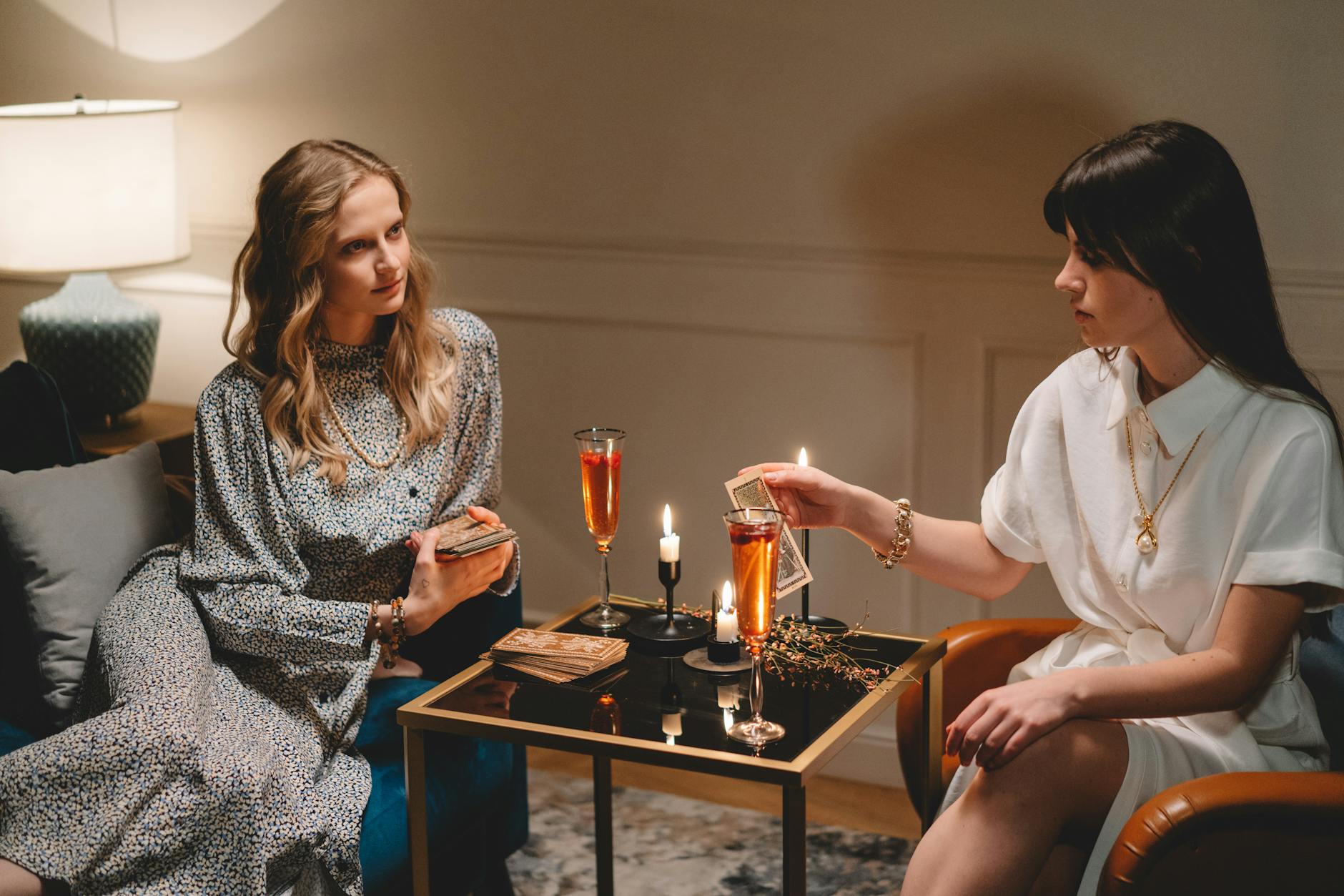 Dwie kobiety przy świecach rozkładają karty tarota w przytulnym pokoju