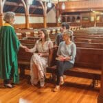 Kapłan w zielonym ornacie rozmawia z wiernymi w drewnianym kościele