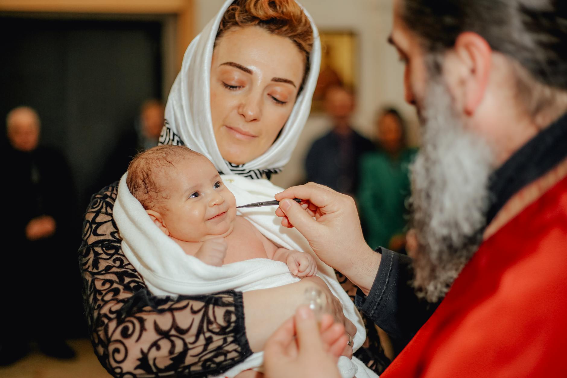 Uśmiechnięte niemowlę podczas chrztu na rękach mamy w chuście