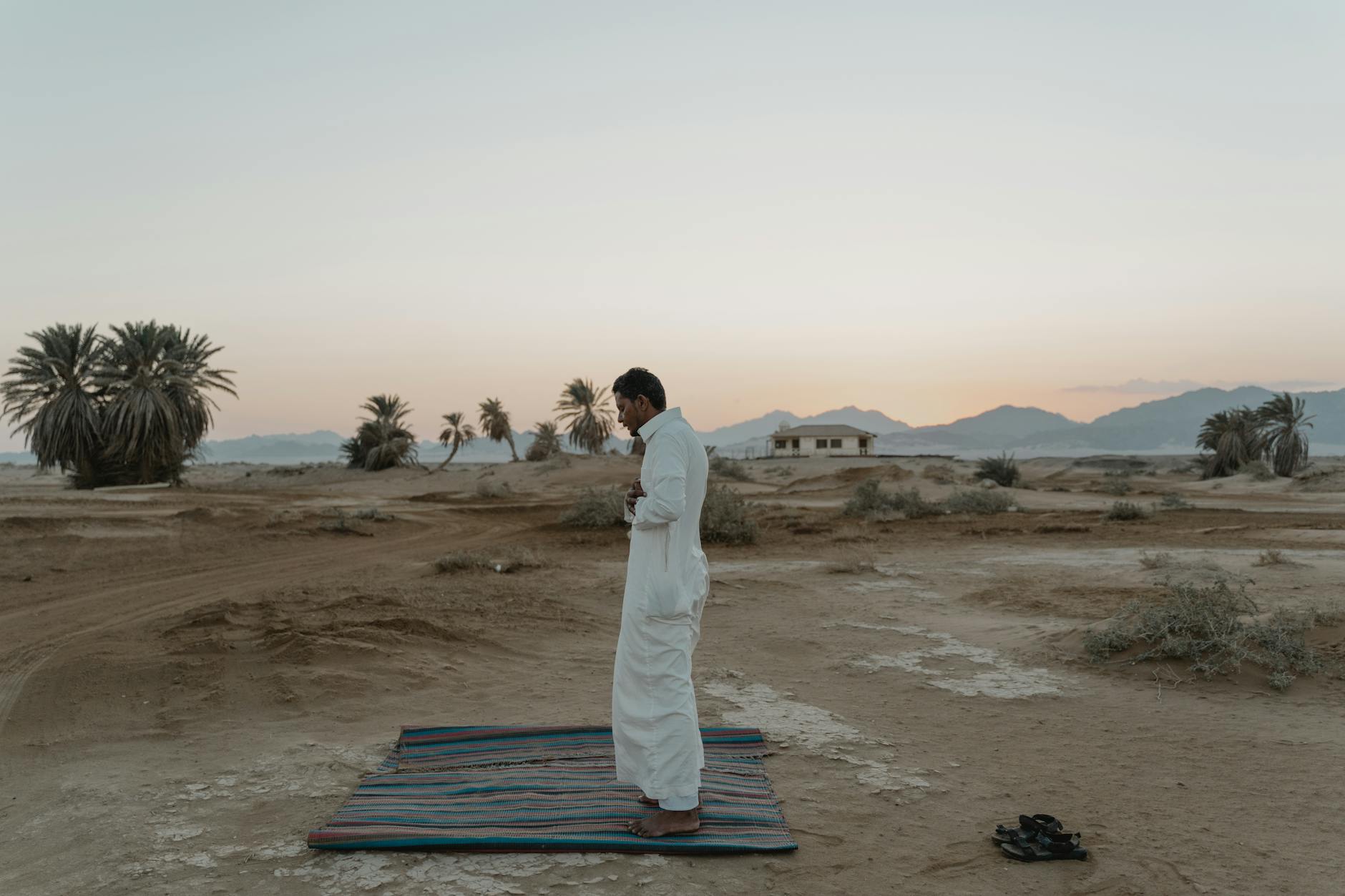 Mężczyzna modlący się na dywanie w pustynnym krajobrazie o wschodzie słońca