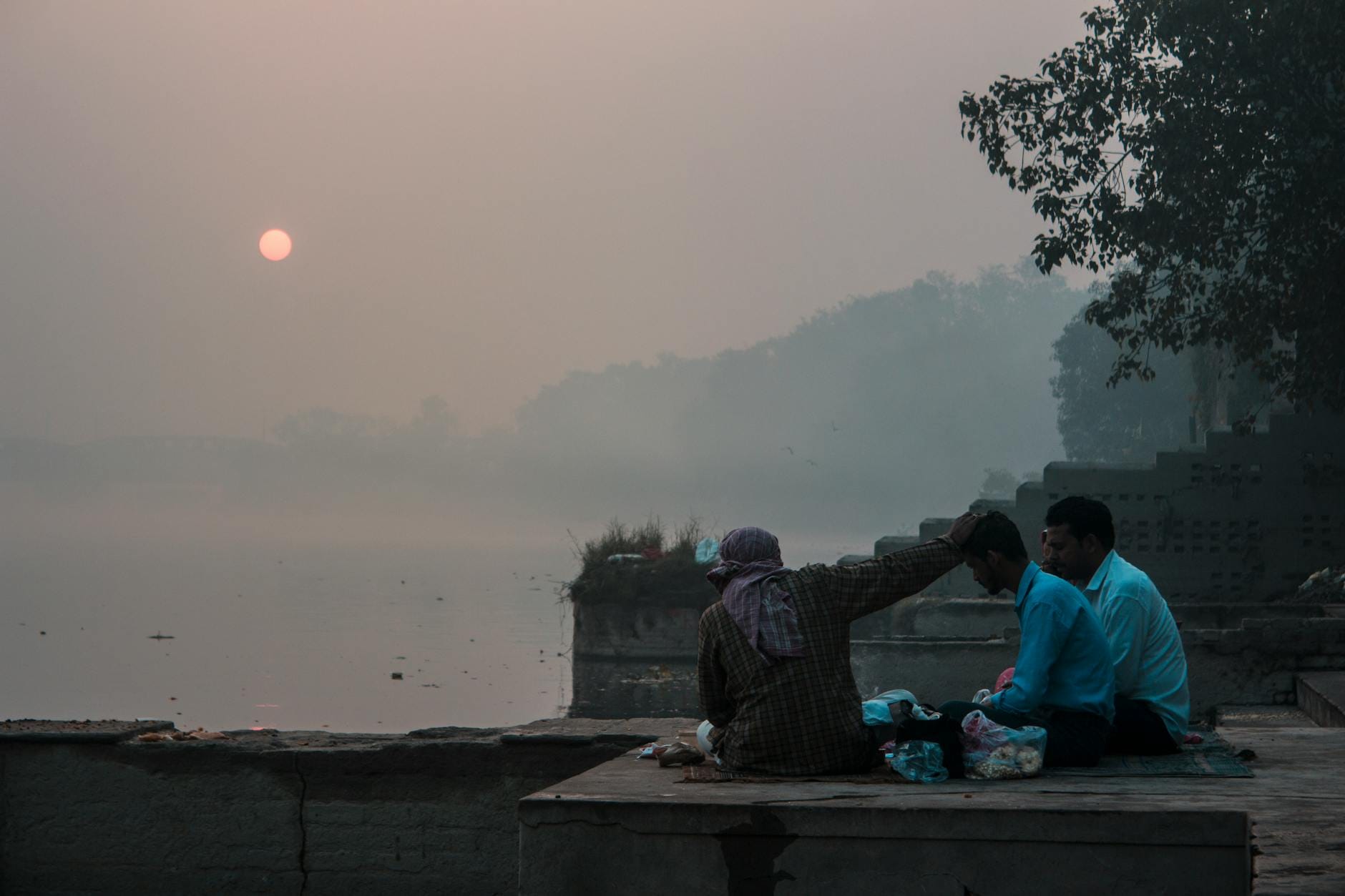 Trzech mężczyzn modli się o świcie nad mglistym brzegiem rzeki w Indiach
