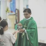 Co oznaczają kolory szat liturgicznych i jak łączą się z rytmem roku? Kapłan w zielonych szatach rozdaje Komunię wiernym w kościele