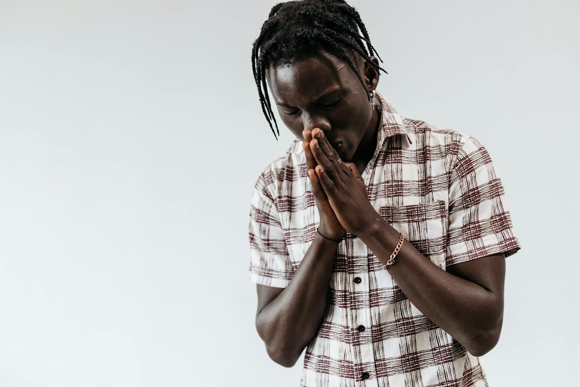 Młody mężczyzna w koszuli w kratę modli się złożonymi dłońmi
