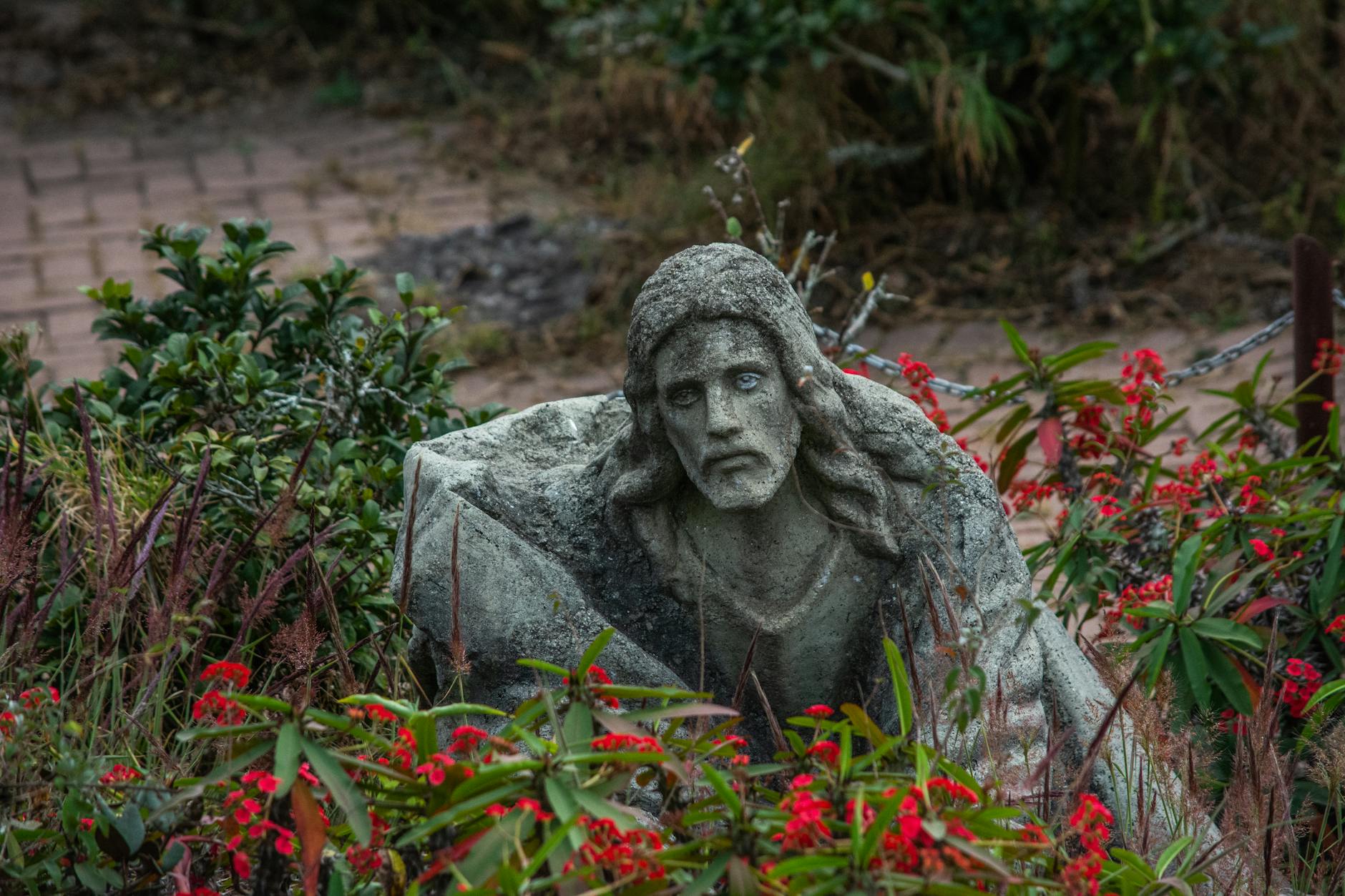 Jezus w Getsemani: „nie moja, lecz Twoja wola” jako droga dla każdego ucznia Kamienna figura Jezusa wśród czerwonych kwiatów w spokojnym ogrodzie