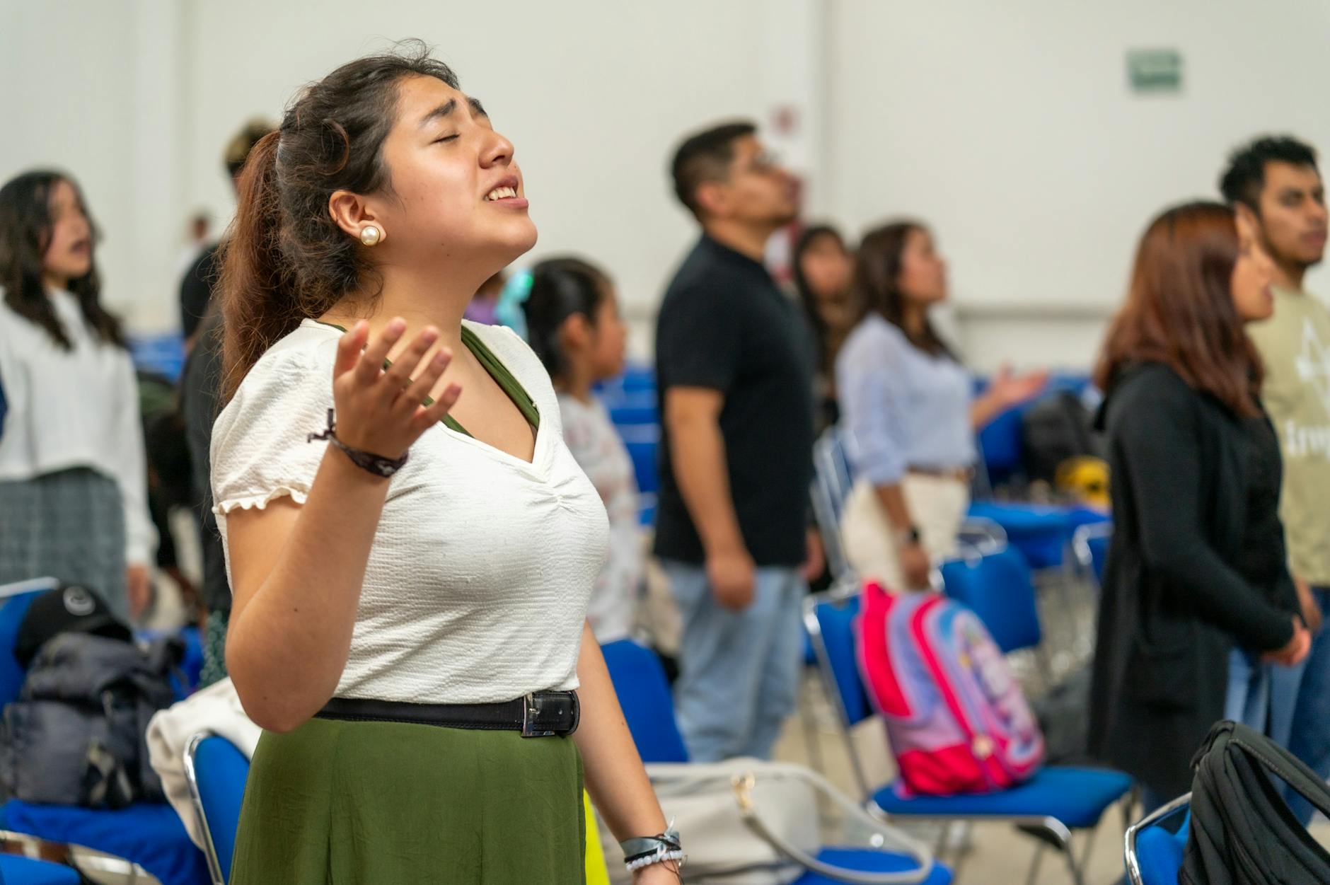 Młodzi dorośli z uniesionymi rękami modlą się razem w sali